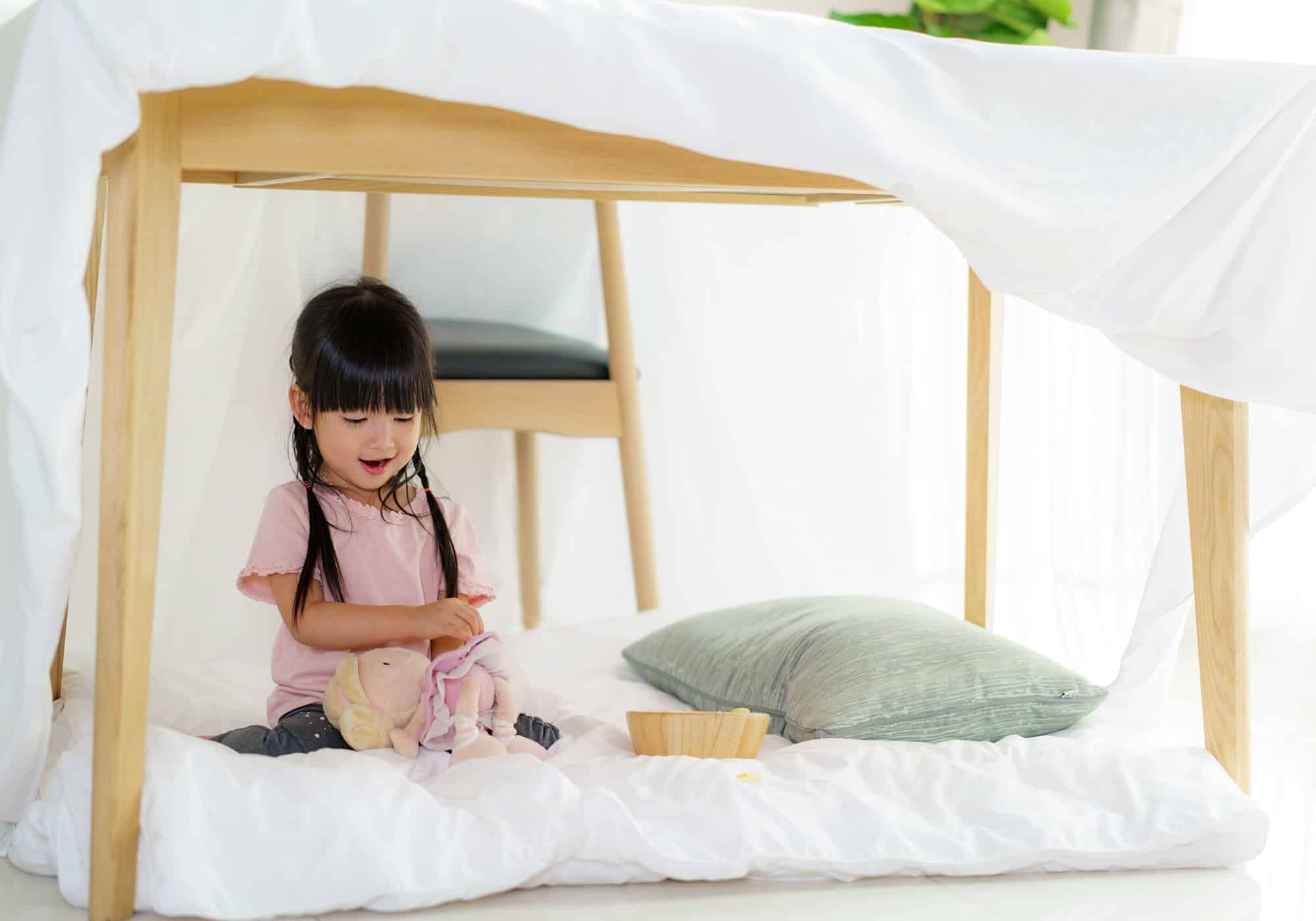 little girl in a fort playing with a doll