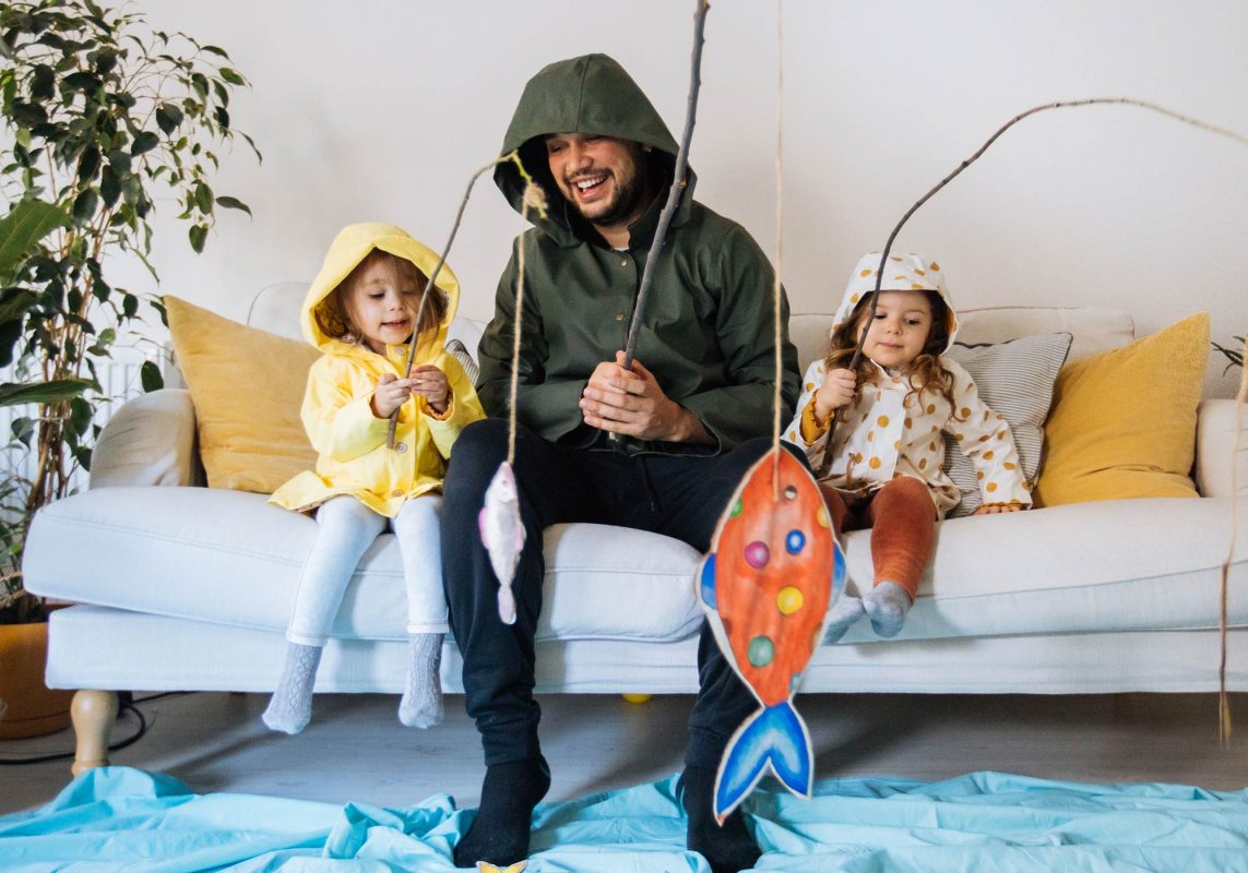 Dad and two young kids on couch pretending to catch fish