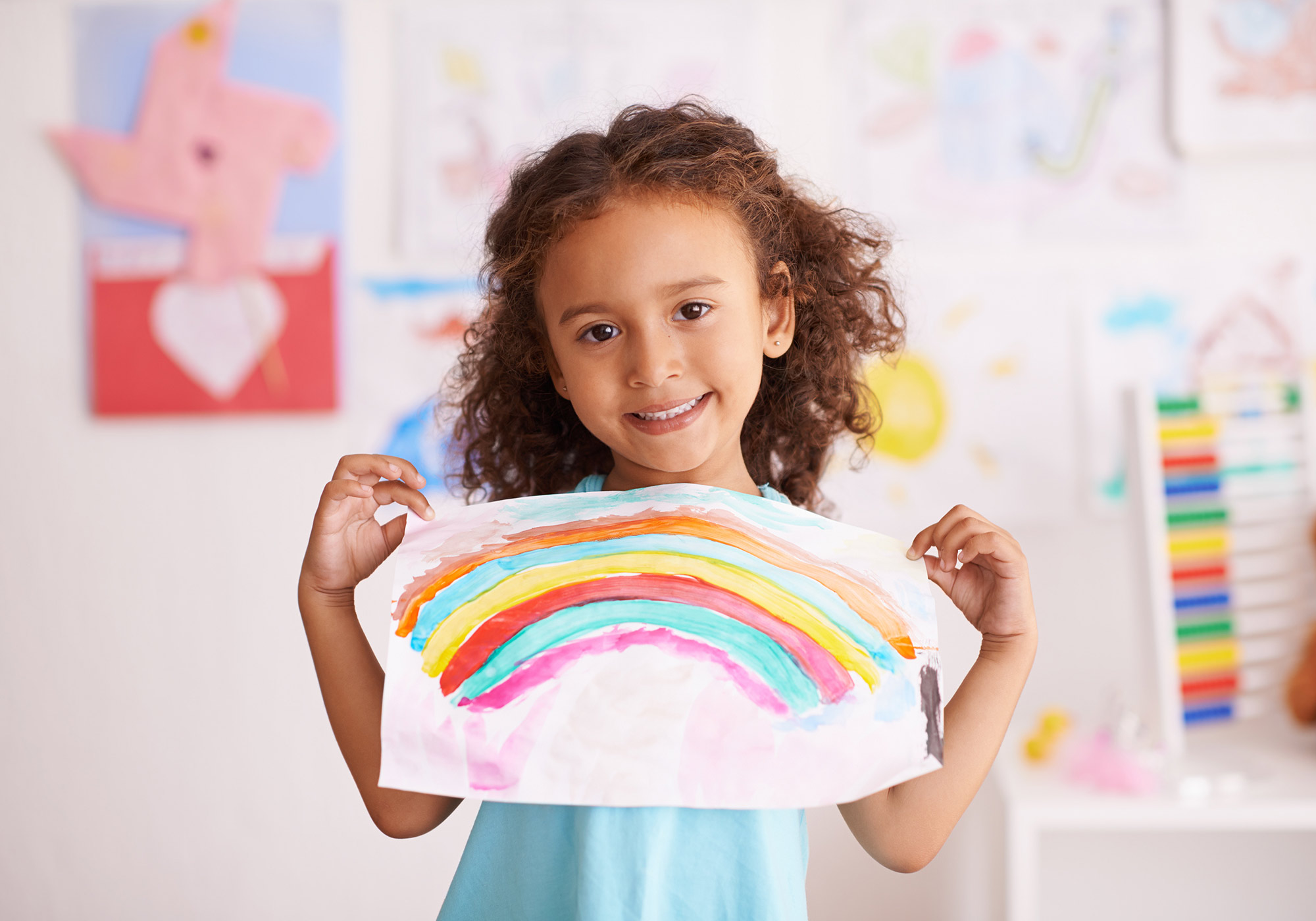 Little girl holding drawing of a rainbow