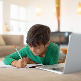 Front view of African american boy using laptop while drawing a sketch on book at home