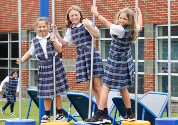 three uniformed girls playing on swings at Charlottesville Catholic School