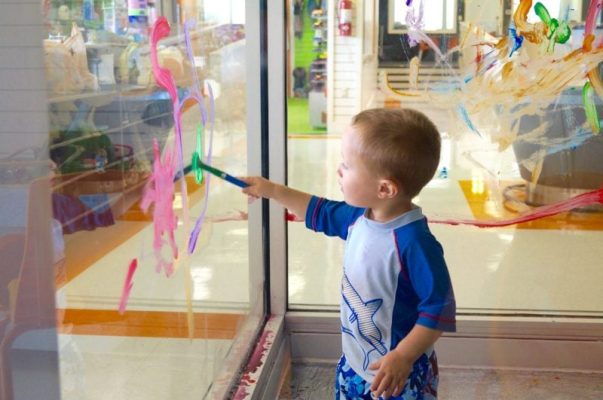 toddler boy painting a window