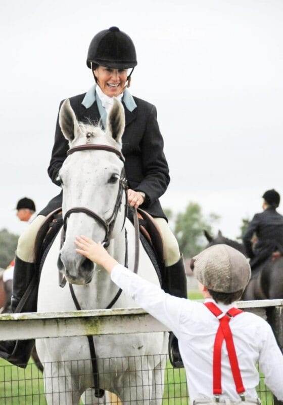Child in suspenders pets white horse at Foxfield steeplechase in Charlottesville