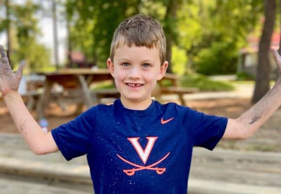 Happy boy wearing a UVA cavaliers shirt, muddy fun at free union school summer camp near charlottesville
