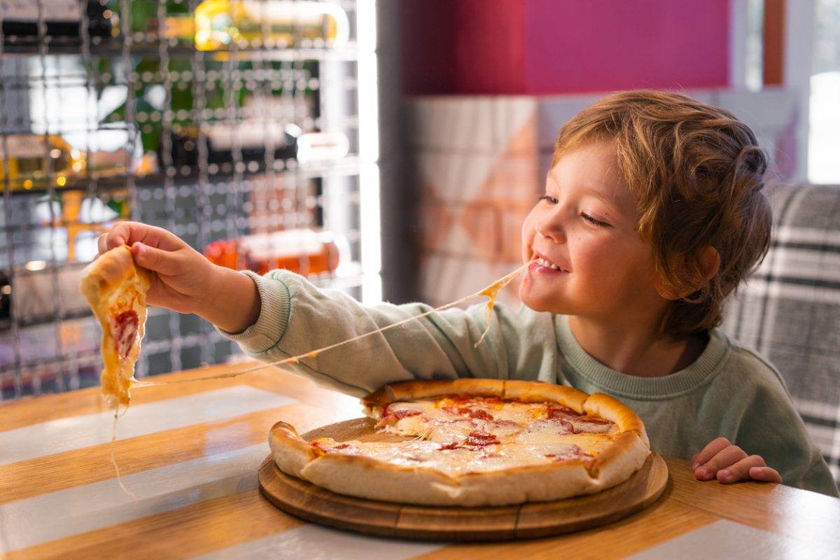Cute boy eating a piece of pizza at restaurant.