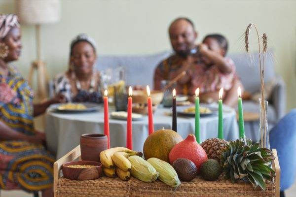 Close-up of traditional decoration with candles and exotic fruits for Kwanzaa celebration with family having dinner in background 