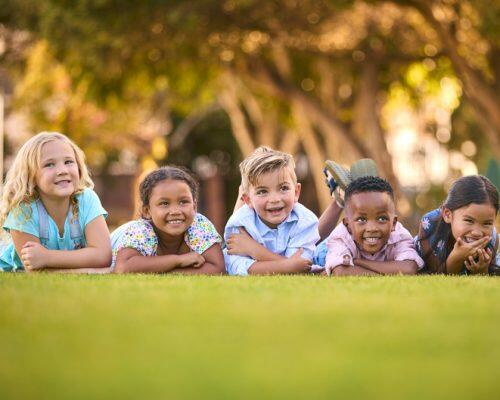 Portrait Of Multi-Cultural Primary Or Elementary School Student Friends Lying On Grass Outdoors