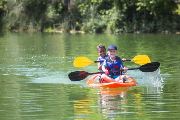 Two young boys kayaking down a beautiful river. Smiling and having fun together on a warm day at summer camp