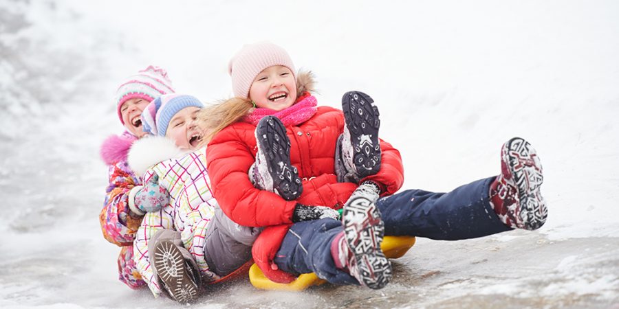 3 kids smiling and sledding in snow