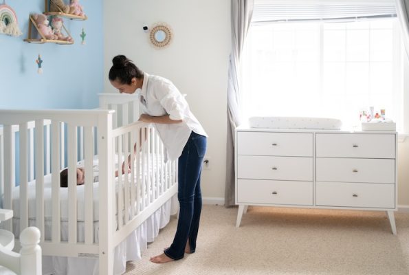 Mom comforting child in crib who is sleeping safely on their back
