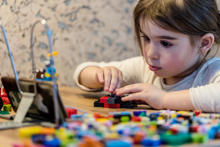 young girl building with lego blocks using instructions on a phone