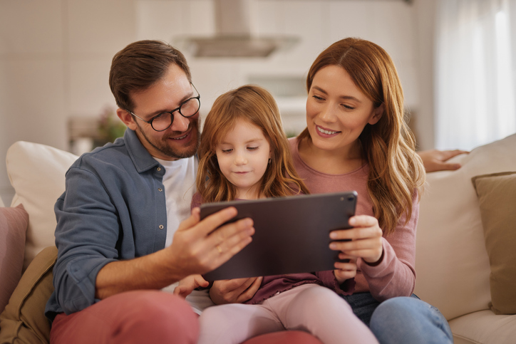 Curious little girl using the tablet with her parents in the living room. parenting and technology.