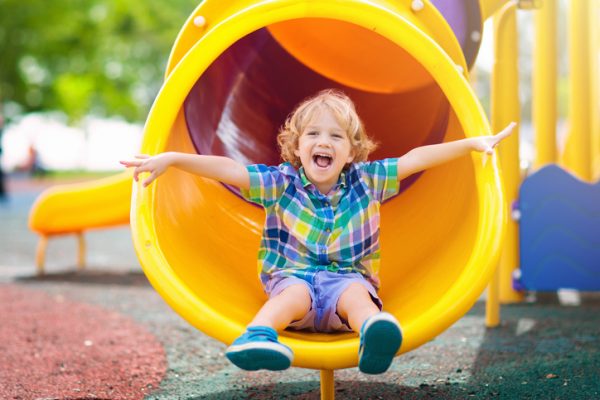 little boy smiling with arms wide at end of big yellow tunnel slide.c