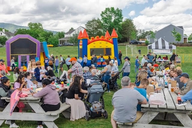 families eating at picnic tables and layout outside with bounce houses in background at Crozet Arts and Crafts Festival